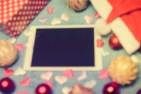 Defocused blurred mobile tablet computer with Santa Claus hat and festive Christmas decoration flat...