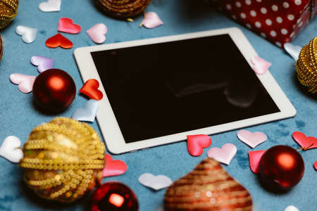 Festive blurry background with white blank tablet mobile computer display and Christmas toys. Mock up top view closeup image of joyful time and technologyの写真素材