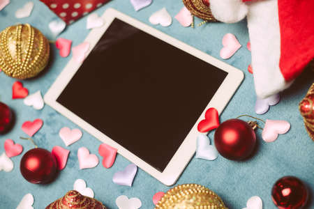 Festive blurry background with white blank tablet mobile computer display and Christmas toys. Mock...