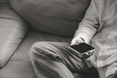 Black and white closeup on mobile phone in hand of man sitting on couch. Top side view mock up backgroundの写真素材