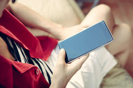 Close up of female hand holding mobile phone with blank screen, light background, top side view