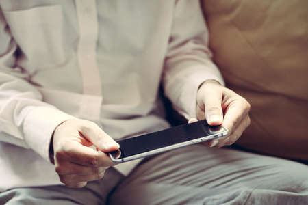 Closeup on mobile phone in hand of man sitting on couch. Top side view mock up background