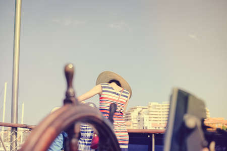 Closeup on steering wheel of sailing ship and back view of mother with kids. Sunny blue sky outdoors background. Book cover idea designの写真素材