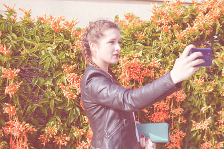 Portrait of young lady using mobile phone taking selfie on outdoor backgroundの写真素材