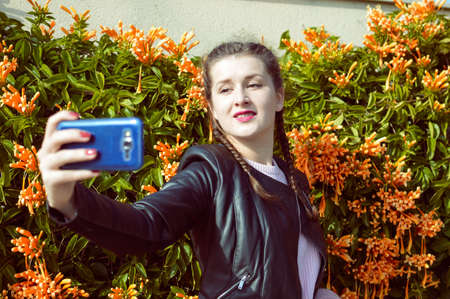 Portrait of young lady using mobile phone taking selfie on outdoor backgroundの写真素材