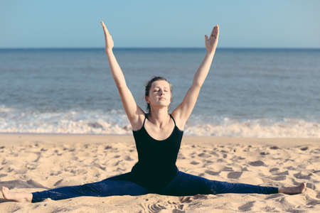 Active young beautiful woman doing stretching exercises on beach sandy outdoors backgroundの写真素材