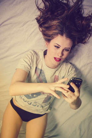 Beautiful woman using mobile phone for texting, calling, making selfie on the bed backgroundの写真素材