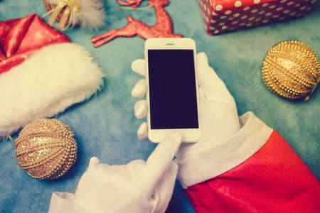 Santa Claus working holding smartphone on festive background. Happy Christmas holiday time design decorationの写真素材