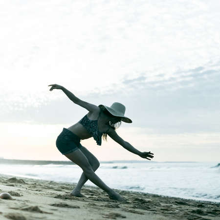 Woman dances barefoot on sand beach on beautiful dawn sky backgroundの写真素材