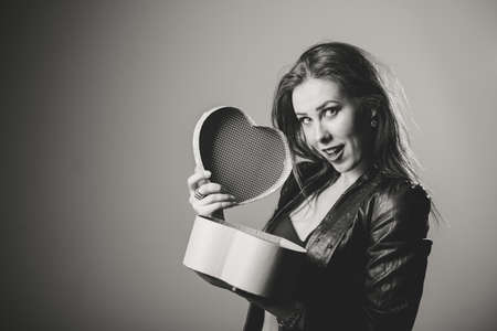 Portrait of beautiful glamorous woman with hands holding love heart shape gift box on light backgroundの写真素材