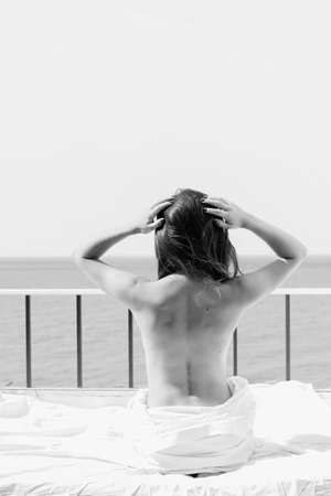 Attractive woman in bed over sunny ocean outdoors background. Luxury holiday travel vacation and lifestyle. Black and white picture, back viewの写真素材