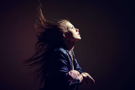 Hot amazing glamorous woman in black leather jacket on light background looking up with blow wind hairの写真素材