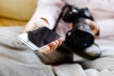 Person using mobile phone and holding DSLR camera in hand on indoors background.の写真素材