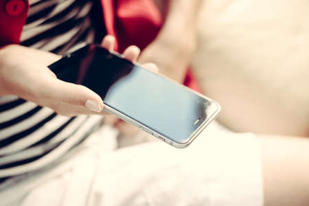 Close up of female hand holding mobile phone with blank screen, light background, top side view