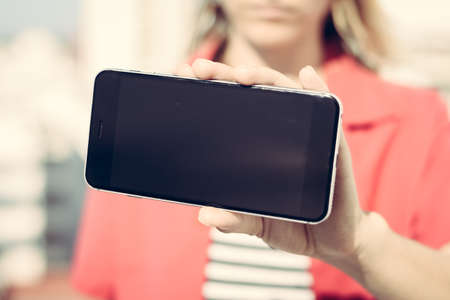 Closeup on mobile phone in hand, blank screen. Blurred outdoor background.の写真素材