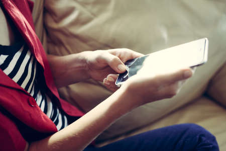 Closeup on mobile phone in hand of young woman sitting on couch. Top side view mock up backgroundの写真素材