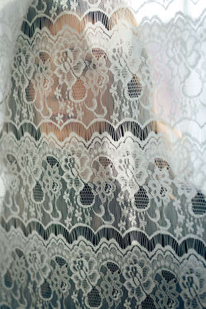 Woman silhouette behind transparent curtain on light window sunny abstract backgroundの写真素材