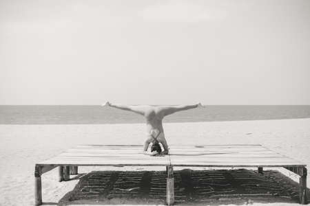 Black and white photography of morning training on the beach. Beautiful female doing workout on sunny outdoors background. Healthy lifestyle exercises. Back side view of perfect fit shape body.の写真素材