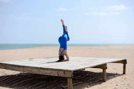 Morning training on the beach. Beautiful female doing workout on sunny blue sky outdoors background. Healthy lifestyle exercises. Back side view of perfect fit shape bodyの写真素材