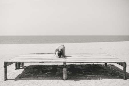 Back view of attractive fit woman stretching over the sea outdoor sunny background. Black and white photographyの写真素材