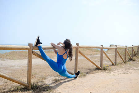 Back view of woman sport stretching over the blue sea outdoor sunny backgroundの写真素材