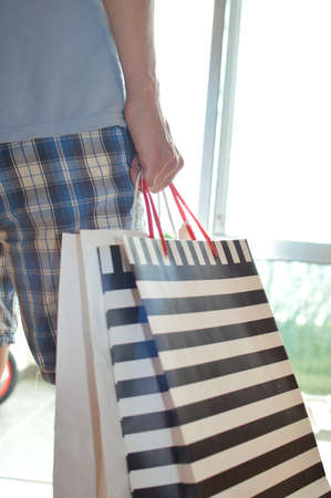 Shopping experience. Close up photography on caucasian male hand holding purchases, light copy space background. Person buying joyful lifestyle.の写真素材