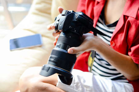Person using mobile phone and holding DSLR camera in hand on indoors background.の写真素材