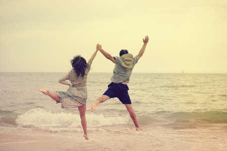 Adult young happy jumping couple on seashore outdoors nature sand background. Back view of pretty...