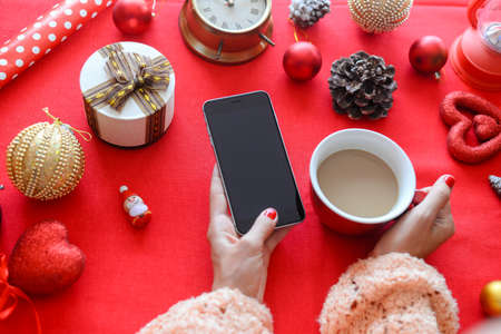 Top side view of hands using mobile phone on red background with Christmas gifts. Xmas Happy New Year composition. Flat lay display design for text message, watching video, game play, wish listの写真素材