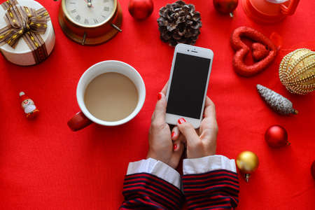 Top side view of hands using mobile phone on red background with Christmas gifts. Xmas Happy New Year composition. Flat lay display design for text message, watching video, game play, wish listの写真素材