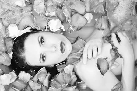 Black and white photography of sexy model with silk skin having fun laying in flower petals bath and looking at camera relaxing on copy space background, close up portraitの写真素材