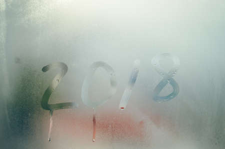 2018 sign draw on wet condensated window glass, blurred texture abstract background, close up view photoの写真素材