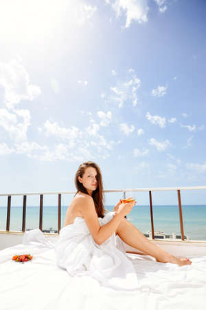 Cheerful beautiful woman enjoying healthy relax lifestyle drinking hot beverage looking out window having positive day and bright sunny oceanfront outdoors background. Travel relaxation destinationの写真素材
