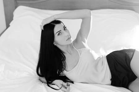 Black and white photography of sexy young pretty lady having fun relaxing lying in bed happy smile over light backgroundの写真素材