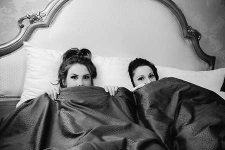Black and white picture of scared friends girls watching horror movie on tv at home laying in bedの写真素材