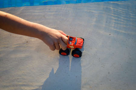 Defocused blurry closeup on child hand playing with car in the water splashing on sunny outdoors...