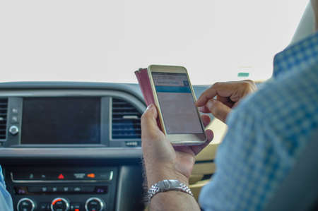 Closeup on person holding using mobile phone on the car interior background, modern smart computer apps solution and online networkの写真素材