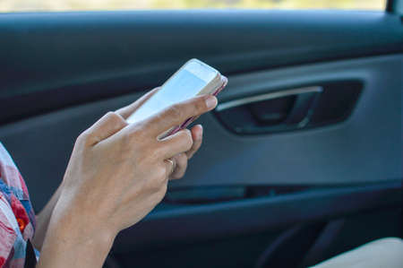 Closeup on person holding using mobile phone on the car interior background, modern smart computer apps solution and online networkの写真素材