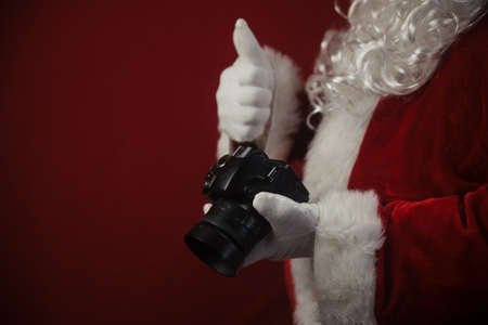 Santa Claus using DSLR camera taking images showing thumb up. Happy Christmas Evening and New Year celebration background. Fun loving creative costume timeの写真素材