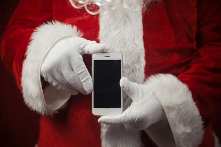 Santa Claus using working on mobile phone. Closeup image of modern communication technology....