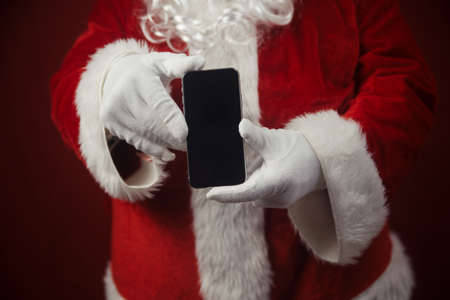 Santa Claus using working on mobile phone. Closeup image of modern communication technology. Telephone call, sending text message, taking photography and filming video during joyful happy timeの写真素材