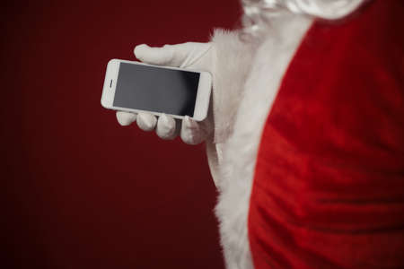 Santa Claus using working on mobile phone. Closeup image of modern communication technology. Telephone call, sending text message, taking photography and filming video during joyful happy timeの写真素材