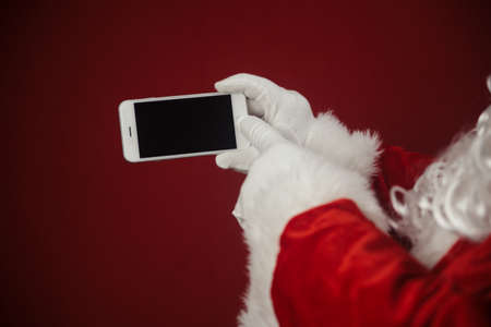 Santa Claus using working on mobile phone. Closeup image of modern communication technology. Telephone call, sending text message, taking photography and filming video during joyful happy timeの写真素材