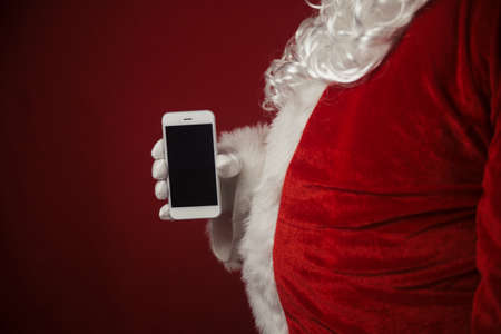 Santa Claus using working on mobile phone. Closeup image of modern communication technology. Telephone call, sending text message, taking photography and filming video during joyful happy timeの写真素材