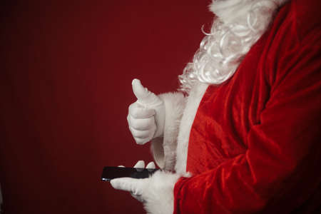 Santa Claus using working on mobile phone. Closeup image of modern communication technology. Telephone call, sending text message, taking photography and filming video during joyful happy timeの写真素材