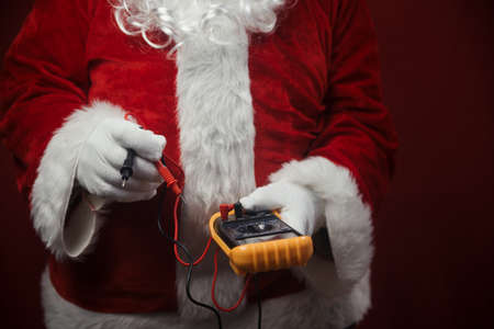 Closeup on Santa Claus solving electricity problems using holding digital tester multimeter electronic measure equipment. Ready for Merry Christmas and Happy New Year celebration backgroundの写真素材