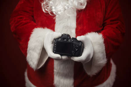 Santa Claus using holding in hands DSLR camera showing screen display. Closeup of creative ideas work, taking shooting images. Happy Christmas and New Year celebration design backgroundの写真素材
