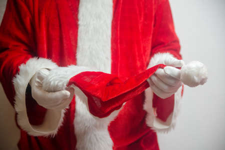 Santa Claus holding in hands red hat on white seasonal background. Ready for festive time. Merry Christmas and Happy New Year close up photographyの写真素材