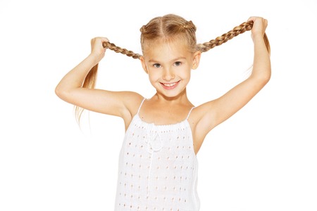 Funny little girl with a charming smile in a white dress holding a pigtailsの写真素材