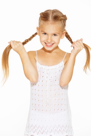 Funny little girl with a charming smile in a white dress holding a pigtailsの写真素材